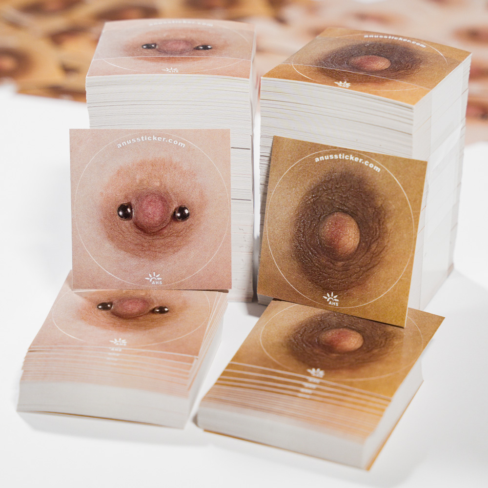Zwei Sticker-Serien mit stilisierten Nippel- und Anus-Motiven in hellen und dunklen Farbtönen, jeweils als dicke Stapel gezeigt